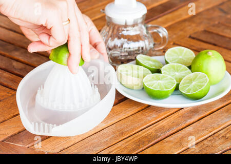 Schiacciamento delle mani di lime fresco sulla tavola di legno Foto Stock