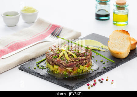 Il tonno rosso tartare di tonno su un nero ardesia piastra con avocado, servita con pane grigliato. Foto Stock