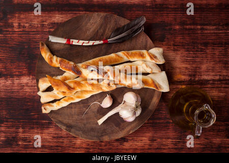 Pizza grissini con aglio e olio di oliva sul tagliere di legno su legno bruno sfondo, vista dall'alto. Gastronomia sfondo. Foto Stock