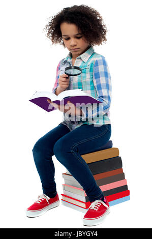Scuola ragazza seduta su un mucchio di libri e lettura Foto Stock