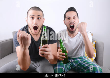 Giovane uomo guarda sport tv con birra e festeggiare. In ambienti chiusi. Foto Stock