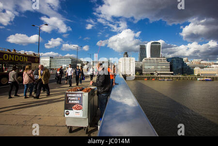 I turisti e la gente del posto si mescolano sul London Bridge sul fiume Tamigi nel sole sotto un cielo drammatico con scudding nuvole riflettono nel ponte ferrovia Foto Stock