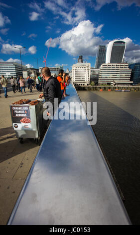 I turisti e la gente del posto si mescolano sul London Bridge sul fiume Tamigi nel sole sotto un cielo drammatico con scudding nuvole riflettono nel ponte ferrovia Foto Stock