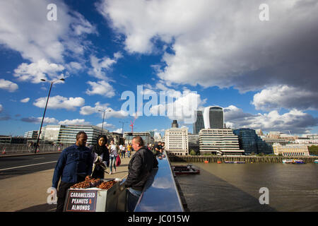 I turisti e la gente del posto si mescolano sul London Bridge sul fiume Tamigi nel sole sotto un cielo drammatico con scudding nuvole riflettono nel ponte ferrovia Foto Stock