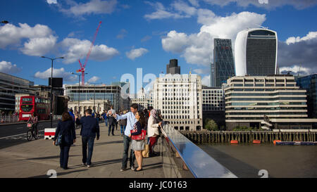 I turisti e la gente del posto si mescolano sul London Bridge sul fiume Tamigi nel sole sotto un cielo drammatico con scudding nuvole riflettono nel ponte ferrovia Foto Stock