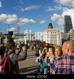 I turisti e la gente del posto si mescolano sul London Bridge sul fiume Tamigi nel sole sotto un cielo drammatico con scudding nuvole riflettono nel ponte ferrovia Foto Stock