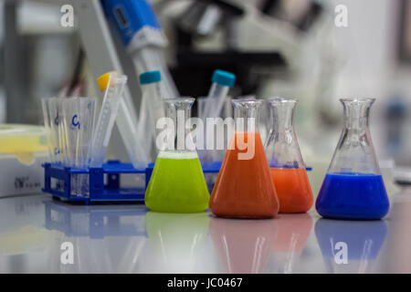 Invenzioni biotecnologiche attrezzature di laboratorio per la ricerca. Flaconi, bottiglie e pipette con colorati arancione verde e blu di liquidi e i campioni di DNA Foto Stock