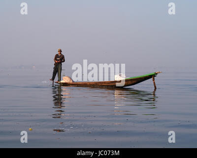 Ragazzo tirando in una rete da pesca su una tradizionale barca sul Lago Inle Myanmar Foto Stock