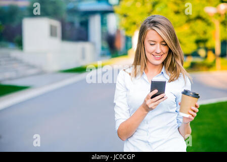 Smart giovane donna professionale la lettura usando il telefono. Imprenditrice femmina per leggere le notizie o i messaggi di testo SMS sullo smartphone mentre si beve il caffè in pausa da Foto Stock