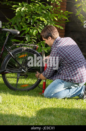 Giovane uomo pompare fino bicicletta pneumatico posteriore in posizione di parcheggio Foto Stock