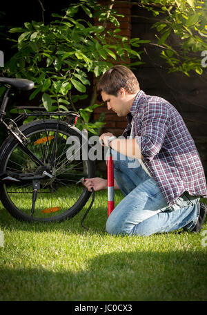 Giovane uomo pompare fino pneumatici sulla sua bicicletta in posizione di parcheggio Foto Stock