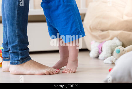 Ingrandimento di foto del bambino in piedi in piedi di fronte a madri i piedi sul pavimento nel soggiorno Foto Stock