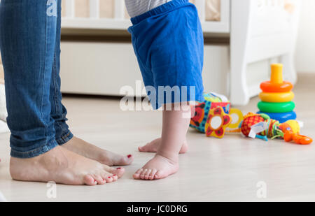 Primo piano del piccolo bimbo con i piedi sul pavimento in salotto accanto alle madri piedi Foto Stock