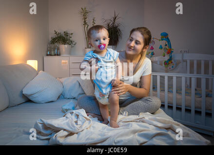 Giovane madre modifica confuso pannolini per il suo bambino sul letto di notte Foto Stock