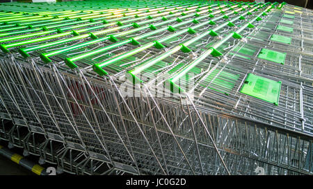 Fila di carrelli di shopping con maniglie verdi nel supermercato Foto Stock