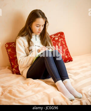 Ragazza seduta sul letto e scrivere poesie in notebook Foto Stock