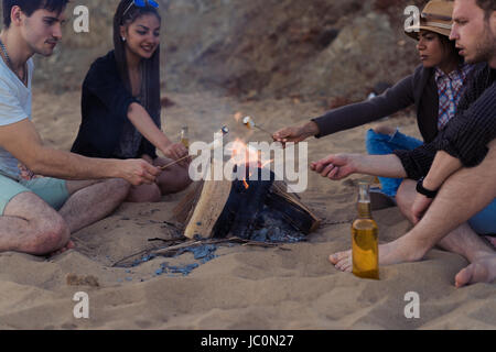 Gli amici su una spiaggia selvaggia acceso un falò e friggere marshmallows Foto Stock