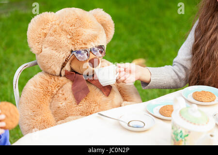Ragazza carina dando il tè di Teddy bear in cantiere Foto Stock