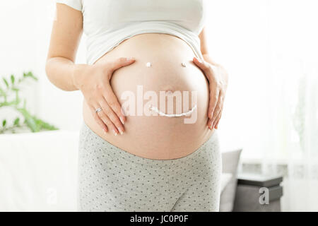 Bella donna incinta con sorriso disegnato da una crema per smagliature sulla pancia Foto Stock