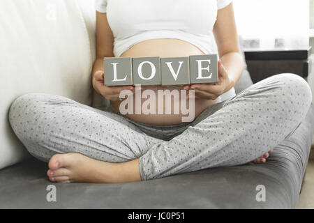 Giovane donna incinta blocchi di trattenimento con lettera rendendo parola amore Foto Stock