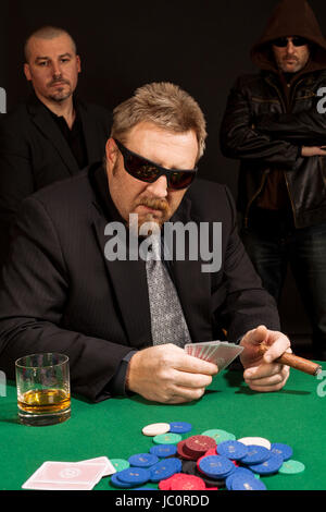 Foto di un uomo giocando a poker indossando occhiali da sole e fumare un sigaro. Foto Stock