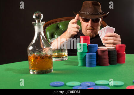 Foto di un uomo giocando a poker indossando occhiali da sole e un cappello. Foto Stock