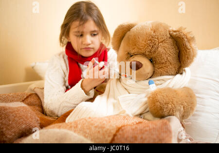 Ritratto di ragazza carina la riproduzione e la misurazione del Teddy bear temperatura con termometro Foto Stock