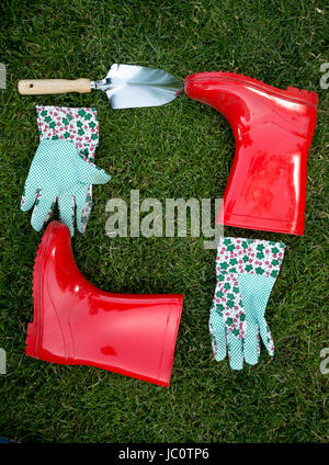 Primo piano di guanti da giardino, spade rosso e stivali di gomma giacente su erba verde Foto Stock