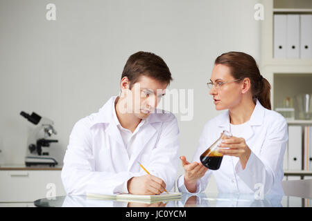 Due scienziati alla ricerca presso lo studio di vetro olio liquido nel pallone in laboratorio mentre analizzando le sue caratteristiche Foto Stock