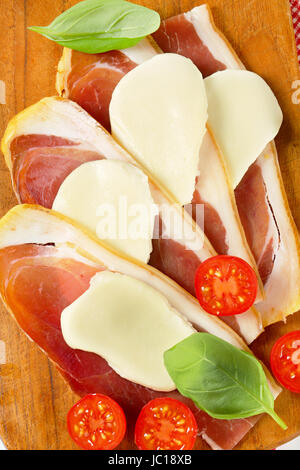 Fette di prosciutto crudo e mozzarella con basilico fresco e pomodori Foto Stock