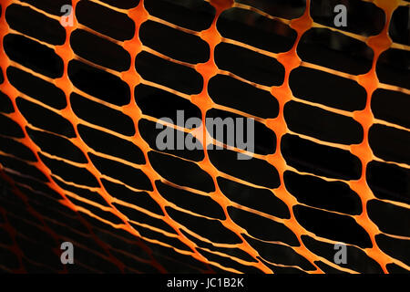 Flessibile arancione costruzione recinzione di barriera, fatta di plastica crea un interessante reticolo quando fotografato vicino e retroilluminato in sun. Foto Stock