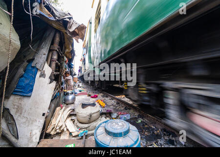 Il numero di abitazioni e di capanne in Cina bazar delle baraccopoli sono situati proprio accanto ai binari della ferrovia, un treno è passante Foto Stock