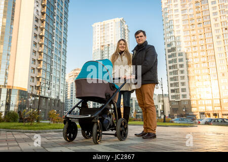 Felice famiglia giovane a piedi con la PRAM su strada al giorno di sole Foto Stock