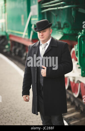 Tonica ritratto di uomo bello in tuta e cappello bowler in attesa del treno Foto Stock