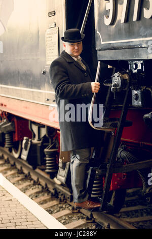 Tonica foto di un uomo in tuta retrò e cappello bowler arrivare in treno vecchio Foto Stock