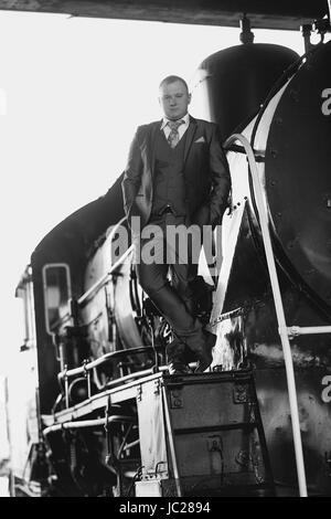 Foto in bianco e nero del giovane uomo in tuta retrò permanente sulla vecchia locomotiva Foto Stock