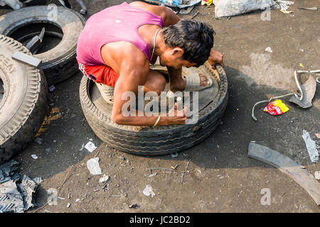 Un uomo è riciclabile di taglio di materiali in gomma da pneumatici per camion in dhapa garbage dump Foto Stock