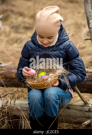 Ragazza sorridente in foresta guardando colorate uova di Pasqua nel cestello Foto Stock