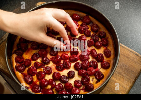 Closeup colpo di mano femminile mettendo le ciliegie sulla sommità della cheesecake Foto Stock