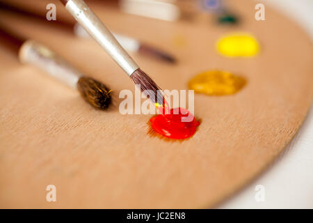 Primo piano del pennello professionale immerso in olio rosso di vernice sulla tavolozza Foto Stock