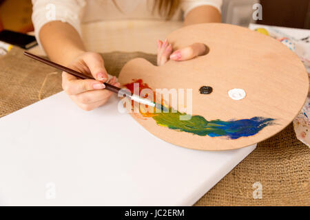 Primo piano della donna artista la miscelazione colori a olio su pallet di legno Foto Stock