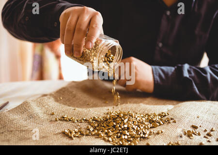 Giovane maschio miner seduta a tavola e versando l'oro dal barattolo di vetro Foto Stock