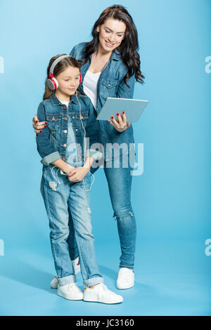 Felice madre e figlia in cuffie utilizzando digitale compressa in studio su blu Foto Stock