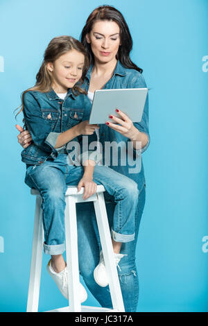 Felice madre e figlia con tavoletta digitale in studio su blu Foto Stock