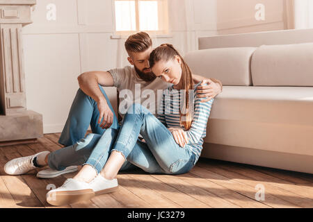 Gara giovane uomo e donna abbracciando e seduto sul pavimento a casa Foto Stock