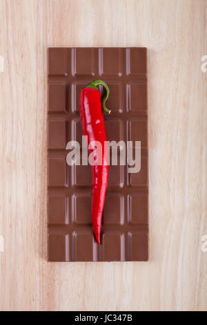 Fresh red hot chili pepper con cioccolato sul tagliere di legno. Foto Stock