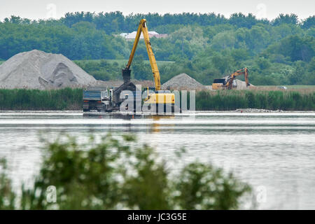 Escavatore caricamento sabbia e ciottoli in un camion su un lago Foto Stock