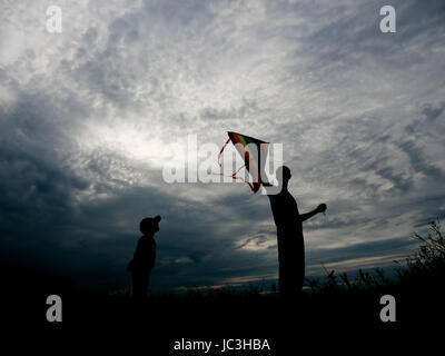 Padre Felice e piccolo figlio di lanciare un aquilone al tramonto Foto Stock