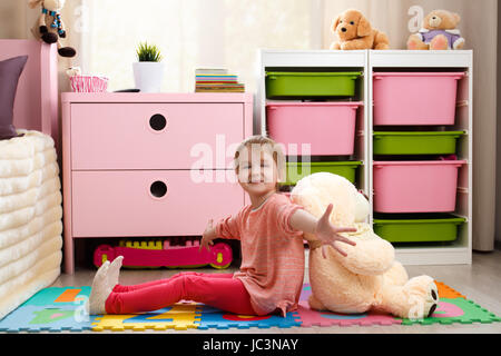 Carino bambina con un grosso orso di peluche seduto sul pavimento nella stanza dei bambini Foto Stock