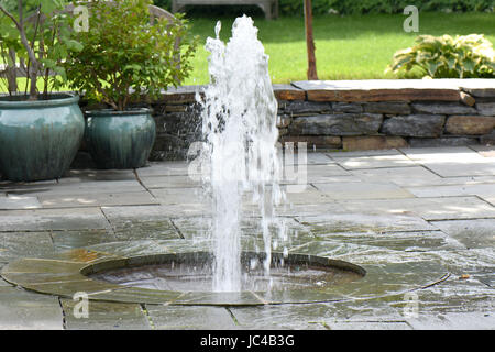 Una formale fontana acqua schizza su un patio in pietra. Foto Stock